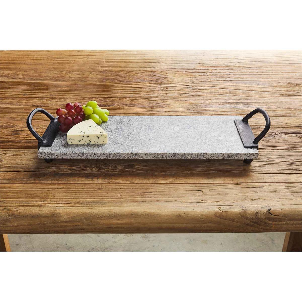 granite handle board displayed on a rustic wood table with purple and green grapes and triangle block of cheese