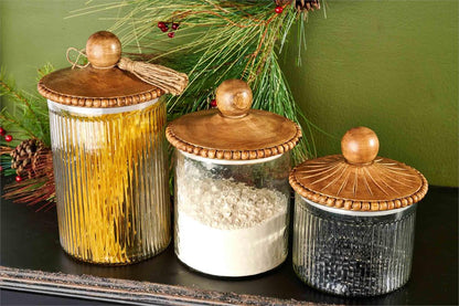 3 sizes of glass canisters with wooden lids filled with dry goods in a row ;on a black table.