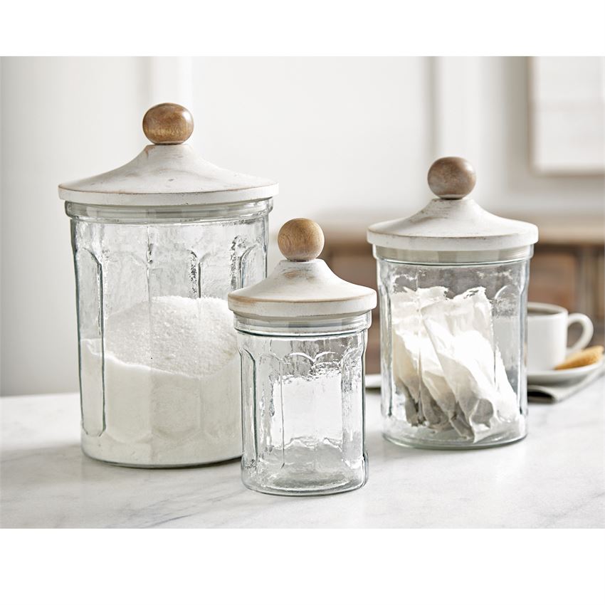 glass canister set displayed on a white countertop next to a cup of coffee