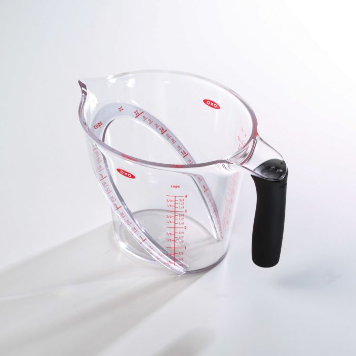 measuring cup with black handle, red markings, and angled rim inside.