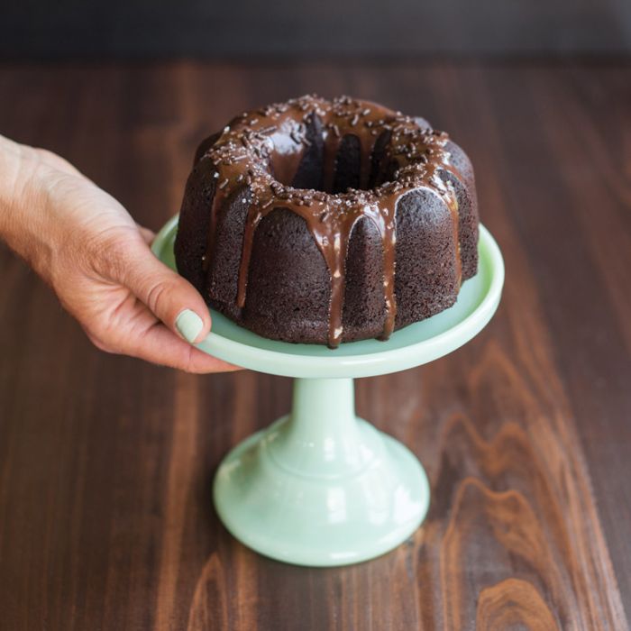 hand holding pedestal with small bundt cake on it.