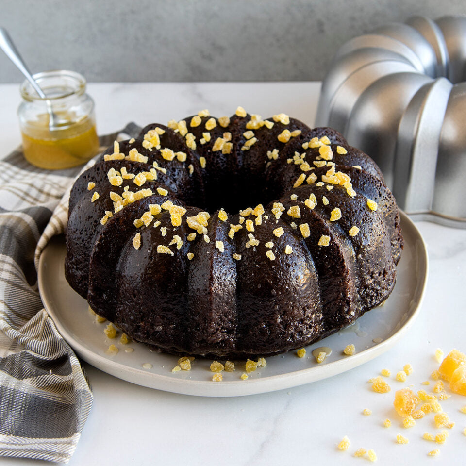 original sparkling silver bundt pan displayed next to a baked chocolate bundt cake next to a towel on a white countertop