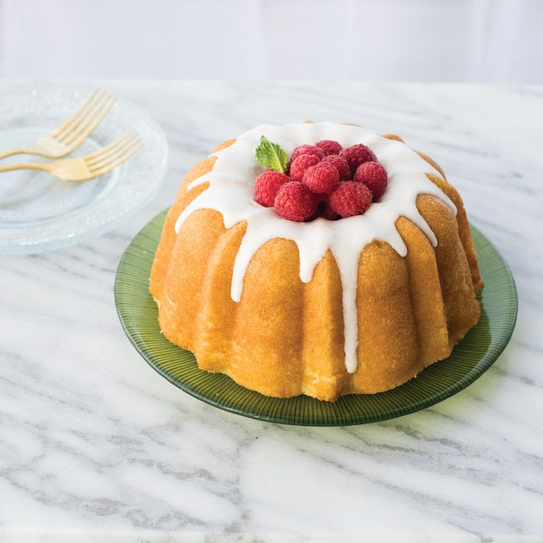 small bundt cake on plate with glaze and raspberries.