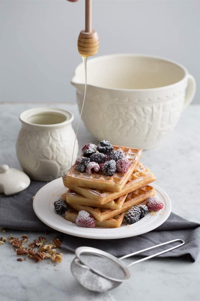 stack of waffles and berries with batter jug in background on marbel countertop.
