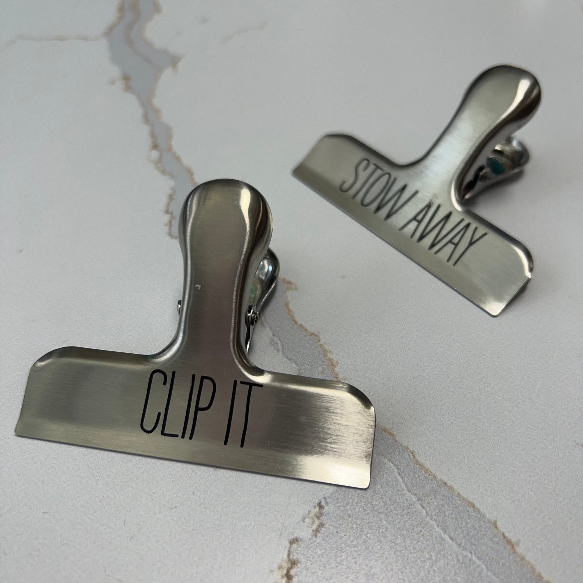 "clip it" and "stow away" bag clips on a white marble counter.