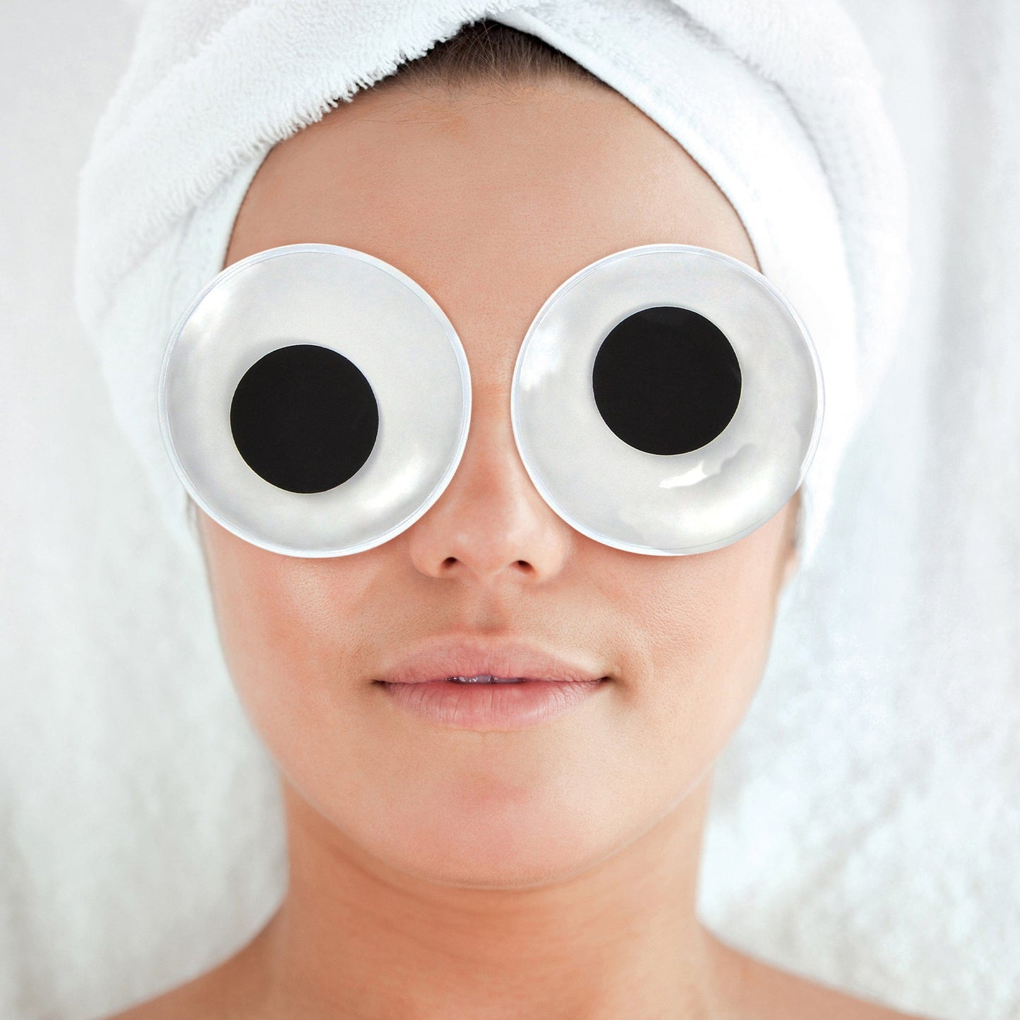 eye pads in the shape giant google eyes laying on a face with hair wrapped in towel