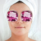 eye pads in the shape of large purple diamonds laying on a face with hair wrapped in towel