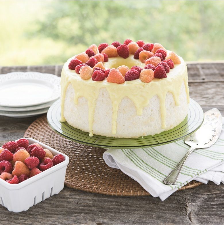angel food cake on pedestal and topped with berries and glaze.