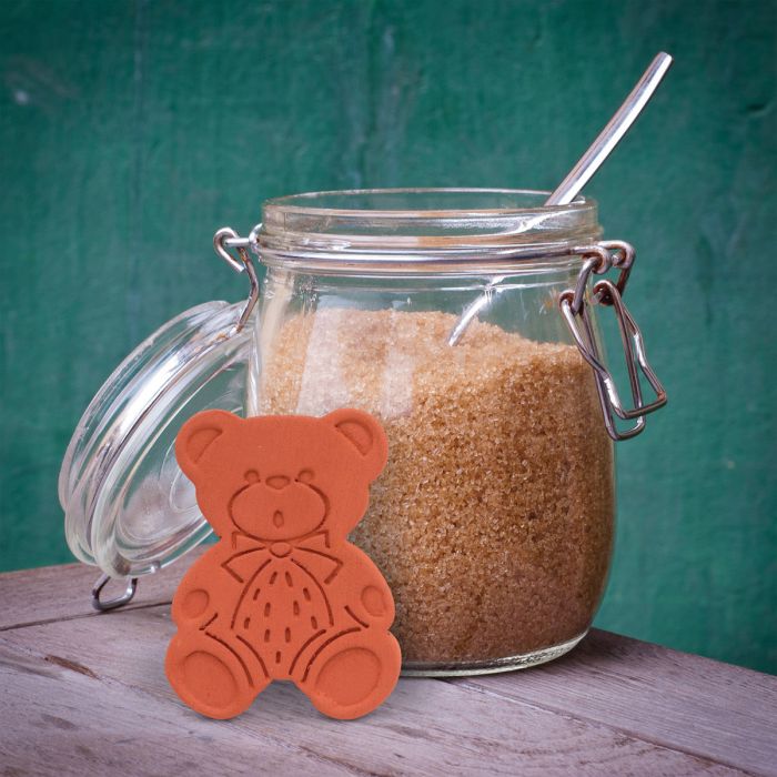 the brown sugar bear displayed next to a opened jar of brown sugar on a rustic wood table against a teal background