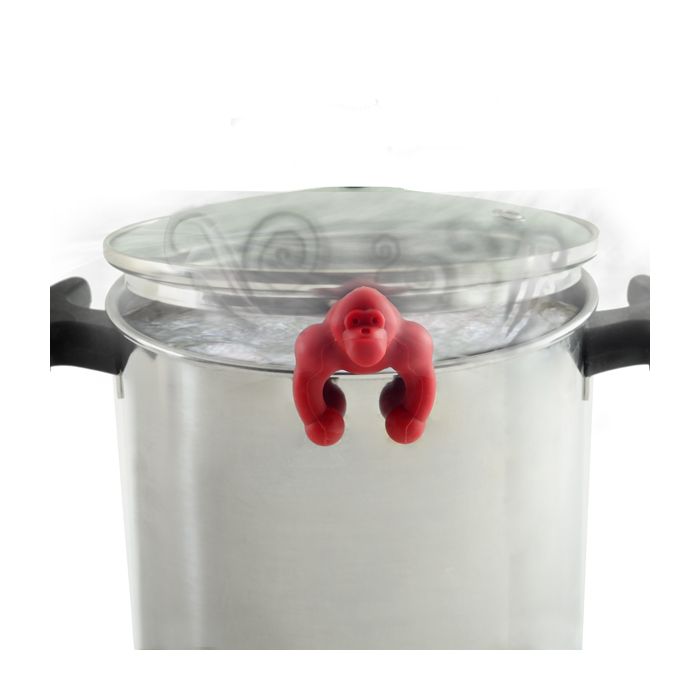 red silicone gorilla resting on edge of pot with lid askew.