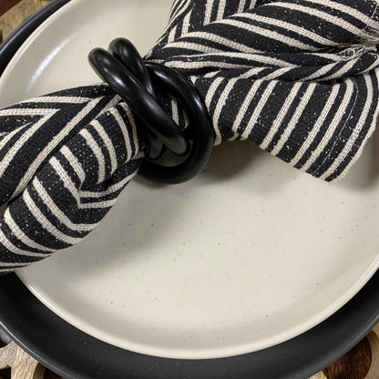 black napkin ring on black and white striped napkin set on plates.