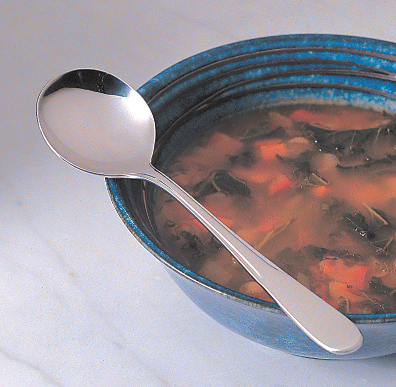 stainless steel soup spoon resting on edge of blue bowl full of minestrone.