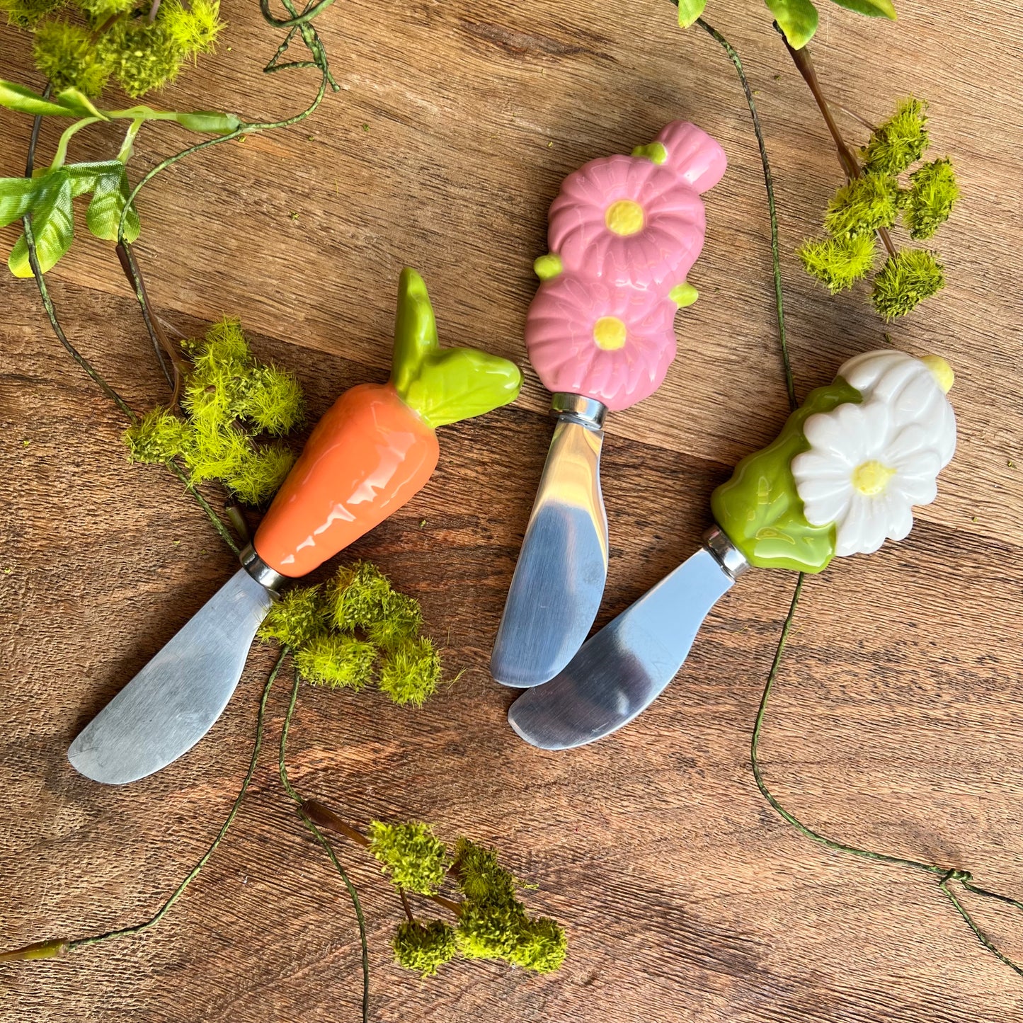 3 ceramic handled spreaders arranged on a wooden background with sprigs of greenery.