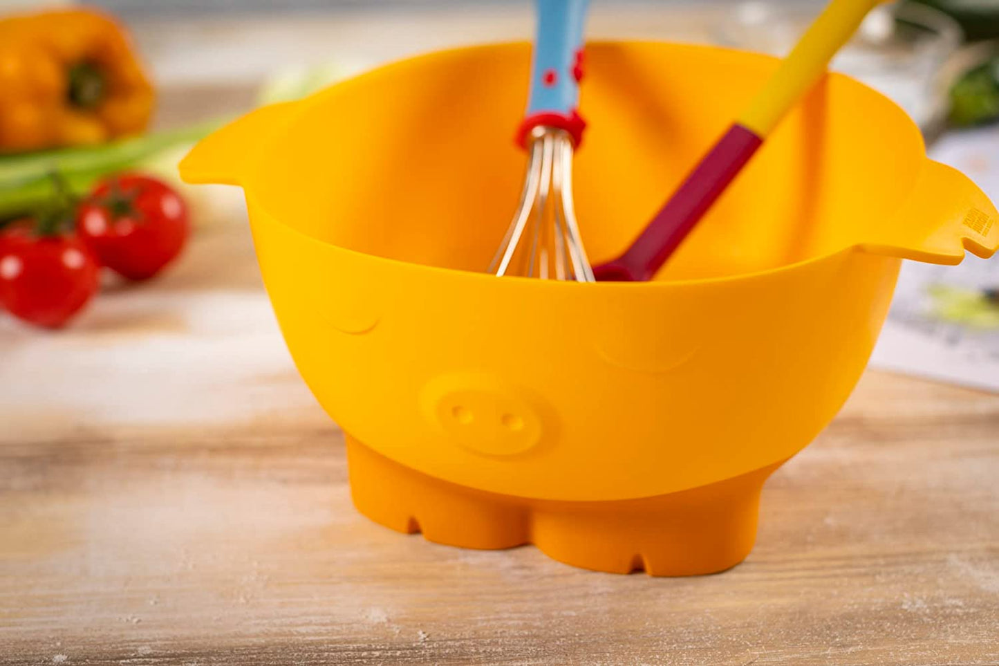 yellow bowl with pig face and feet on a wooden table with spoon and whisk in it.