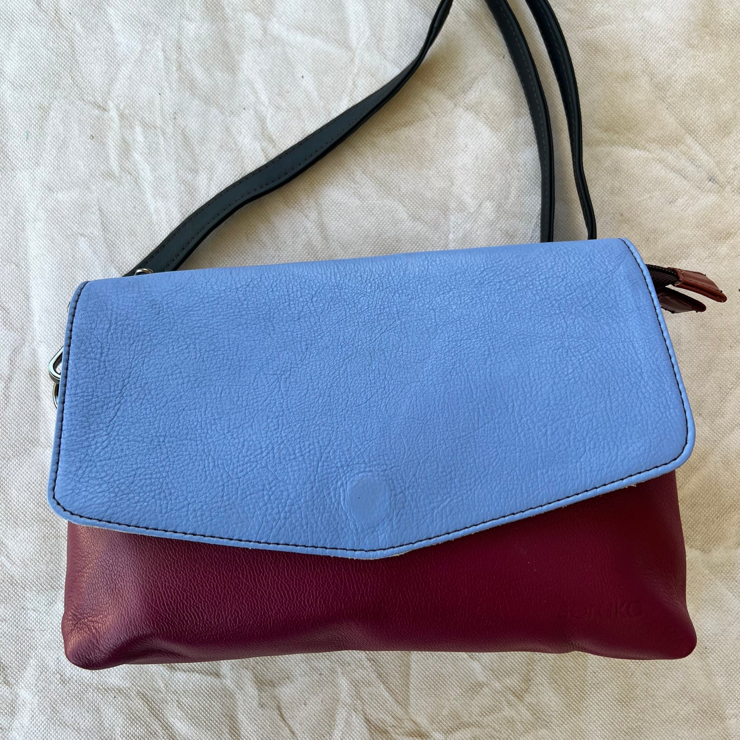 rounded dark pink purse with blue flap and black strap.