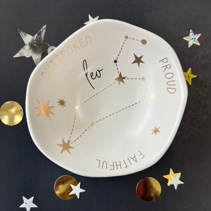 cream dish with gold stars and "Leo Proud Faithful Outspoken" around the inner rim on a black background with scattered stars and orbs.