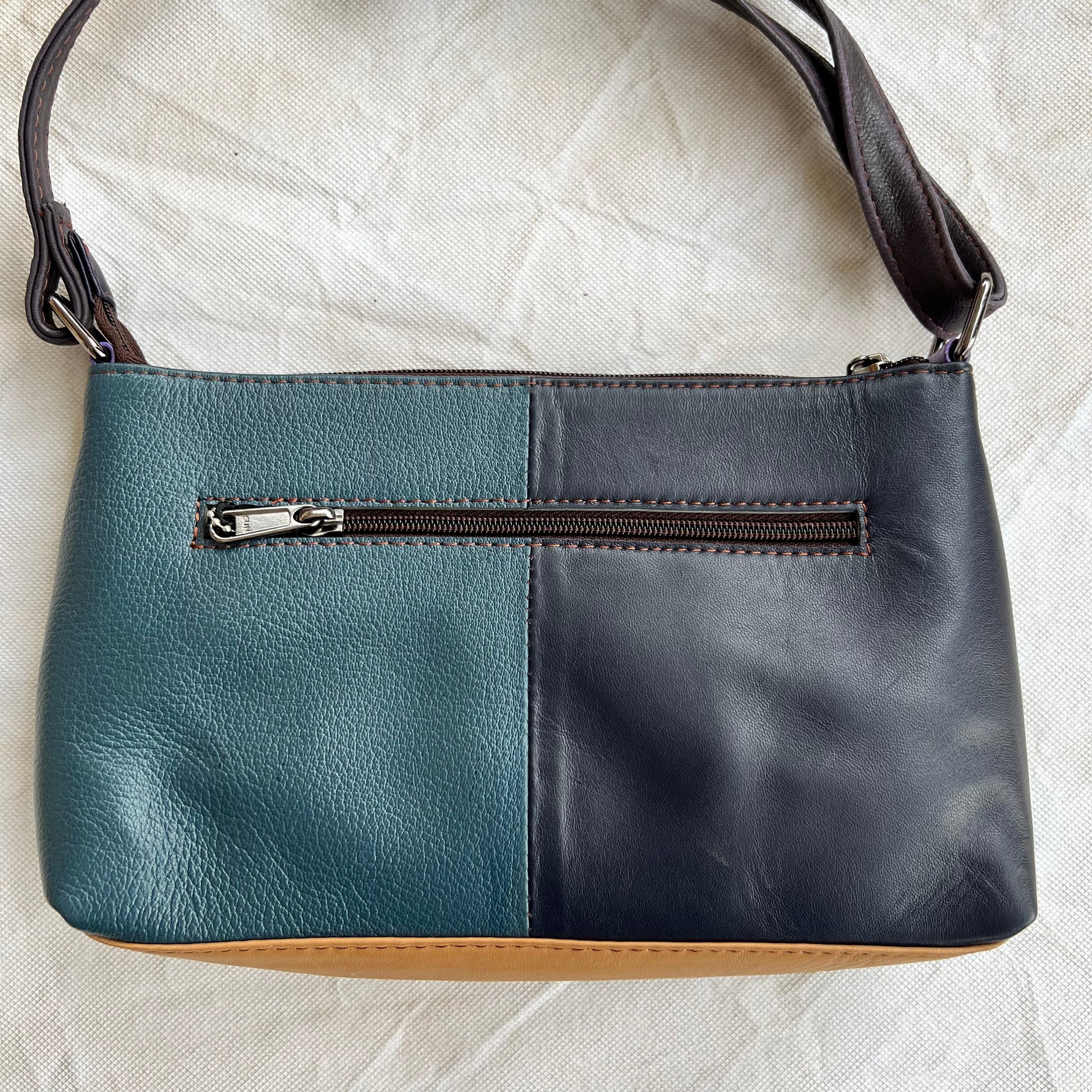 back view of purse that is half blue, half black and has a zipper pocket.