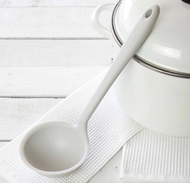 ladle laying on a white dishtowel leaning against a pot on a wooden countertop.