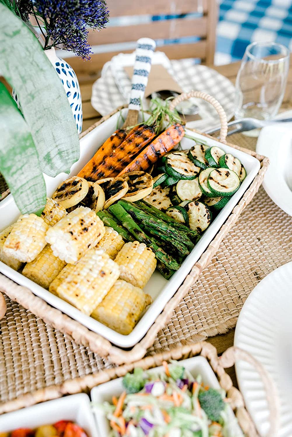 white ceramic baker in a basket filled with grilled veggies on an outdoor table.
