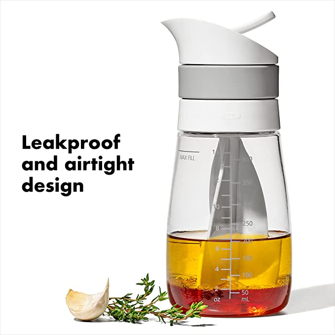 mixer partially filled with vinegar and oil, garlic glove and herbs set next to it, and text "leakproof and airtight design" on a white background.
