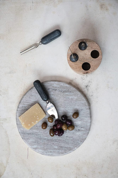 top view of the reversible round marble board displayed with olives cheese and charcuterie utensils on a white marble surface