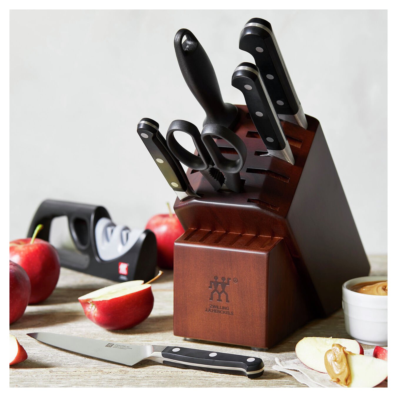 knife block with knives and sharpener on a kitchen countertop with sliced apples.