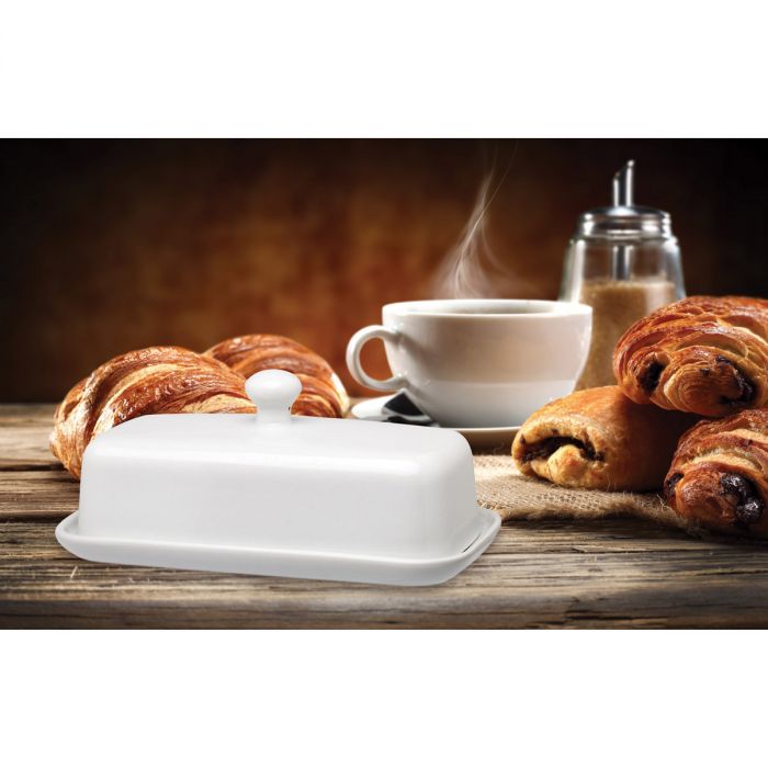 the porcelain butter dish displayed on a rustic wood table with pastries and a cup of coffee