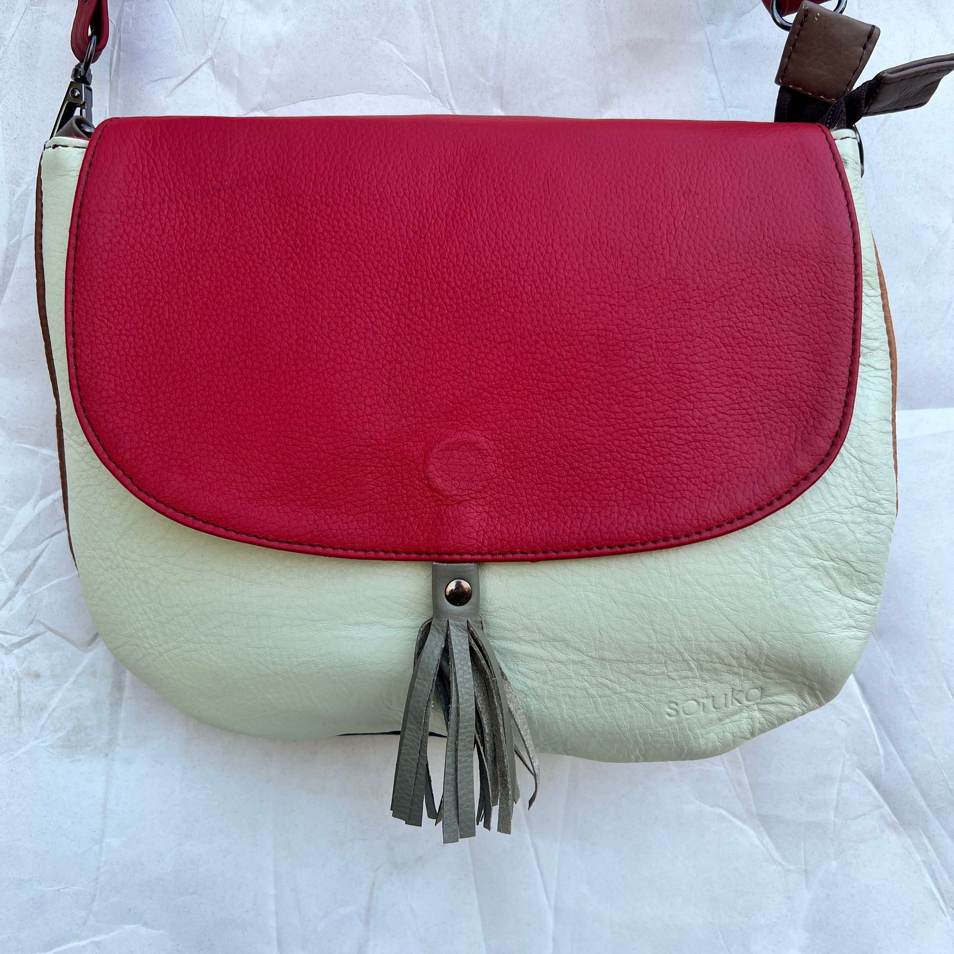 rounded cream purse with red flap, taupe tassel, and red strap.