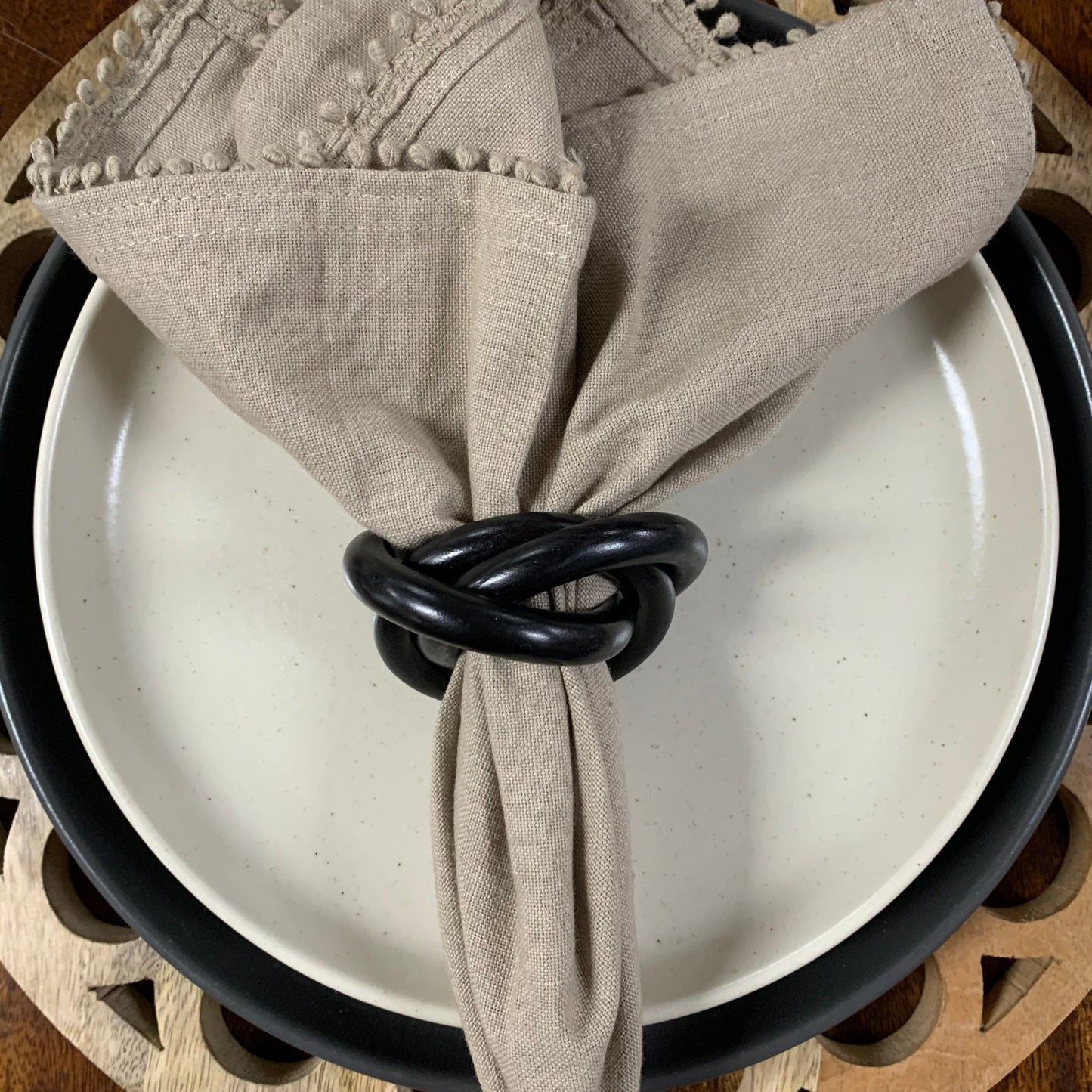black napkin ring on khaki colored napkin set on plates.