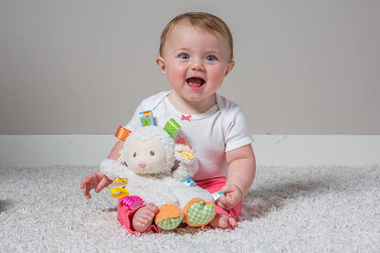 a baby girl sitting on a white rug while holding sherbet lamb lovey stuffed toy