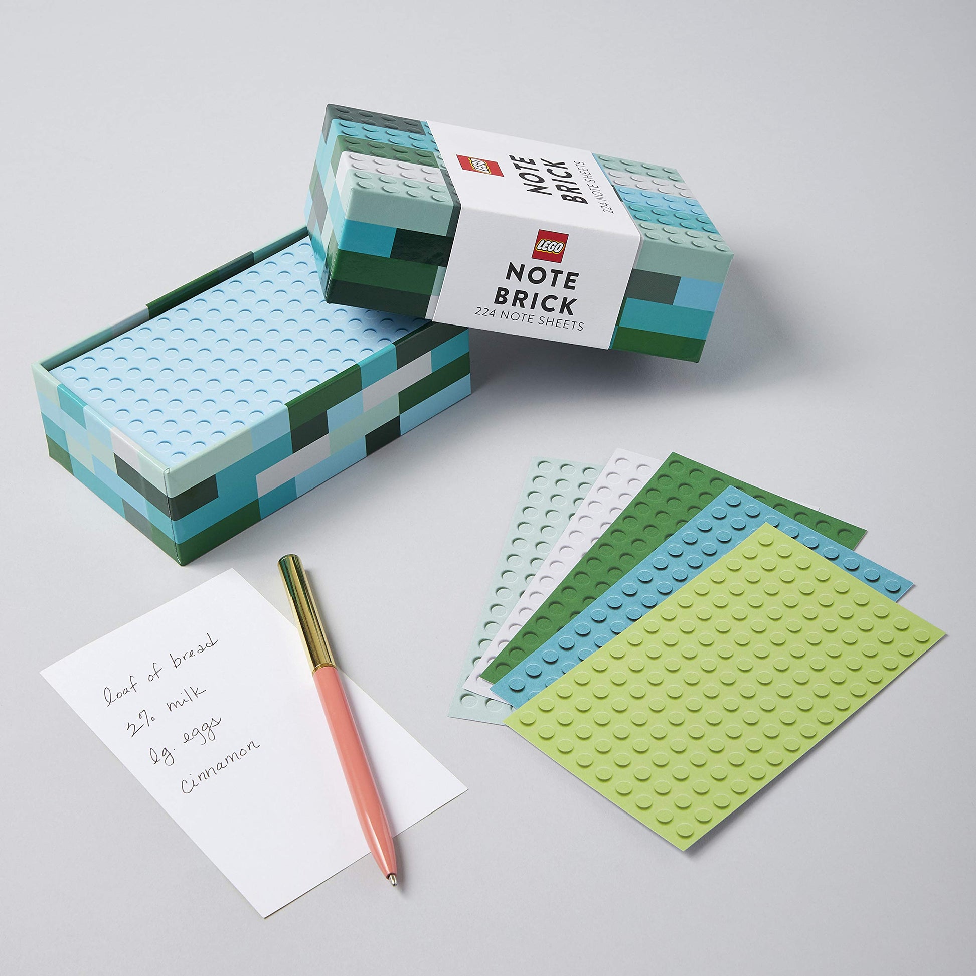 lego designed box with lid off-set to show note paper inside and sheets of note paper with lego design fanned out with a pen.