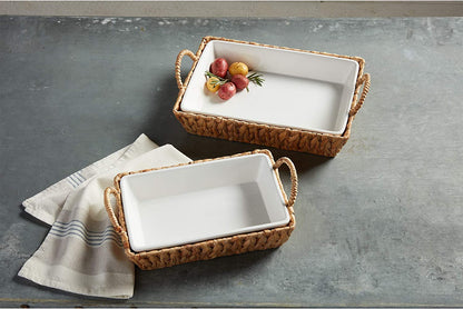 2 sizes of white ceramic bakers set into baskets on a grey table with a dishtowel.