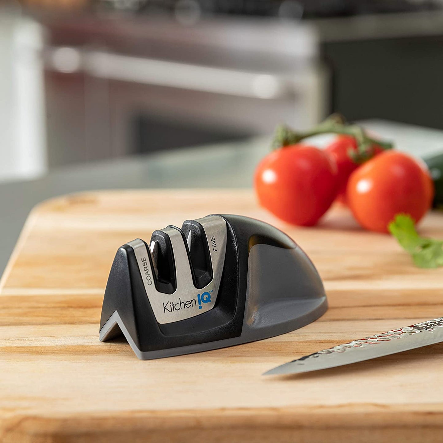 knife sharpener and knife on wood cutting board with tomatoes in background.
