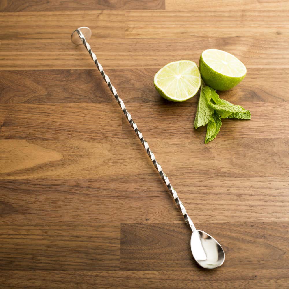 the cocktail mixing spoon displayed on a wooden surface beside cut limes