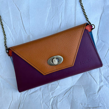 rectangle flat bag with purple and brown leather flap and chain against a light blue background