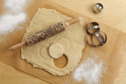 the paisley design rolling pin displayed on a rolled out pastry next to cookie cutters on a wooden surface