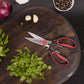 the kitchen shears displayed on a dark stained cutting board next to cilantro and garlic on a black countertop