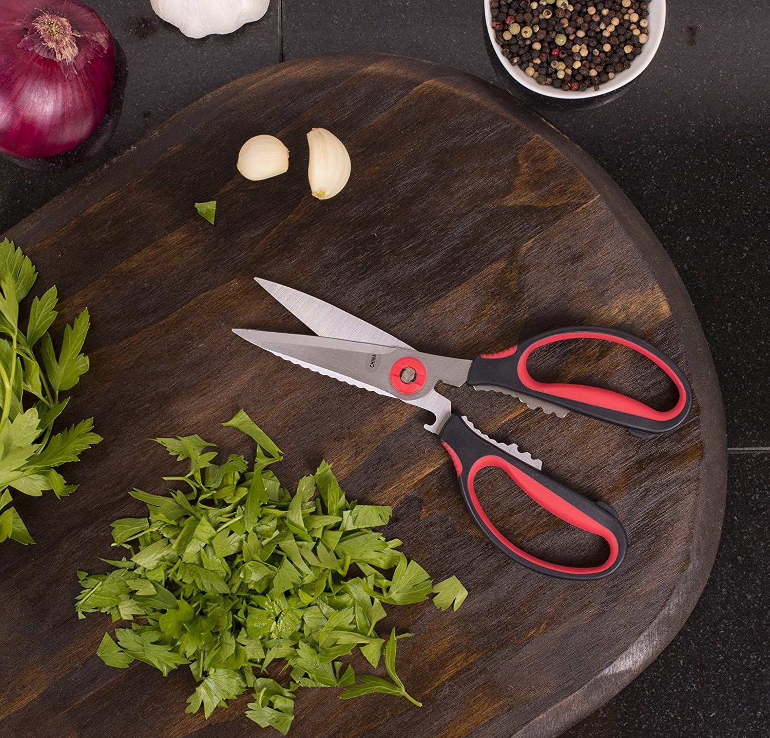 the kitchen shears displayed on a dark stained cutting board next to cilantro and garlic on a black countertop