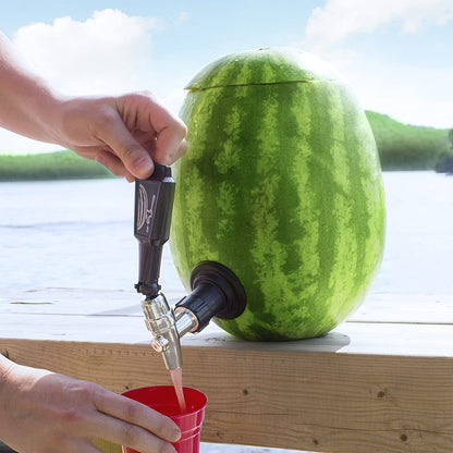 the watermelon keg tapping kit in a watermelon sitting on a table outside while an individual uses it to fill a cup