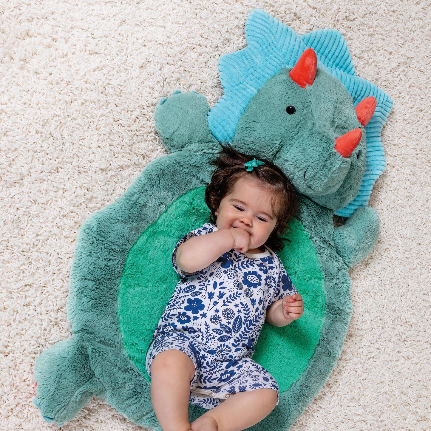 a little girl laying on the pebblesaurus baby mat on a white rug