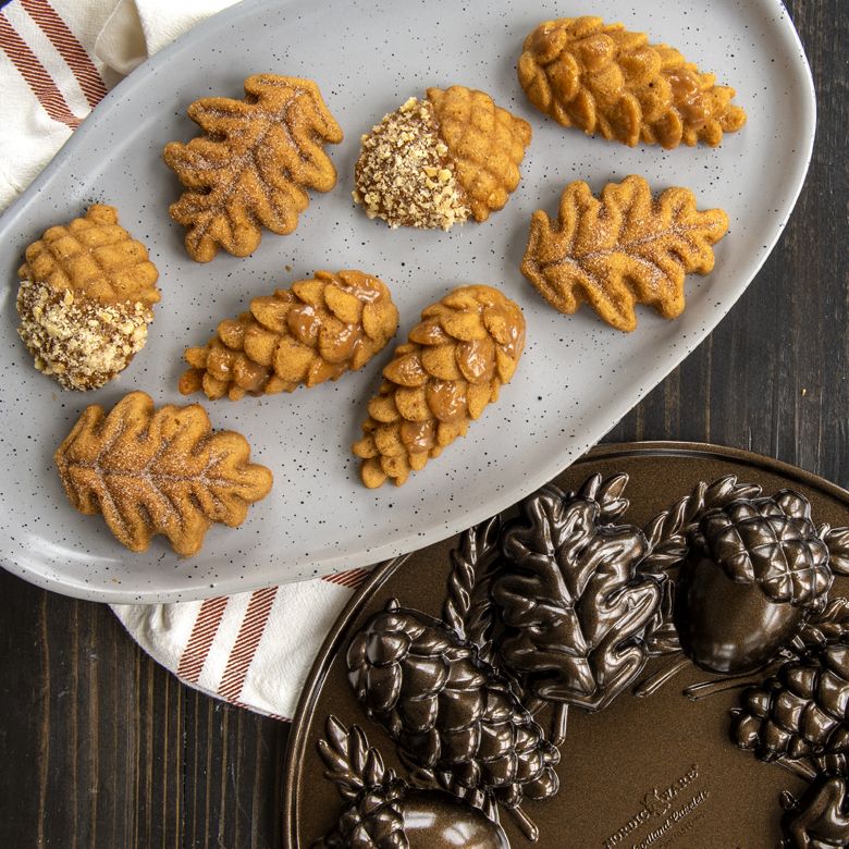 cakelets in shapes of leaves, acorns, and pine cone on tray with pan next to it.