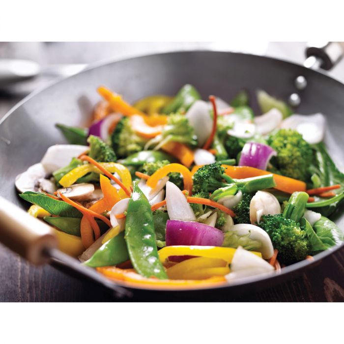 the carbon steel wok displayed with mixed veggies on a dark stained wood surface
