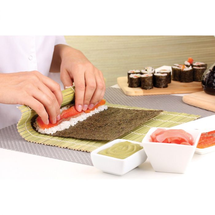 a person illustrating how to use the sushi mat on a white surface surrounded by other ingredients 