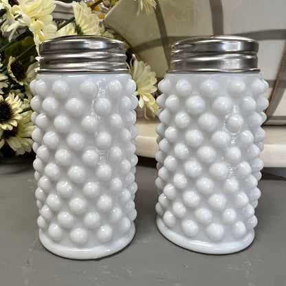 milk glass salt and pepper shakers displayed on a gray surface next to a bundle of flowers