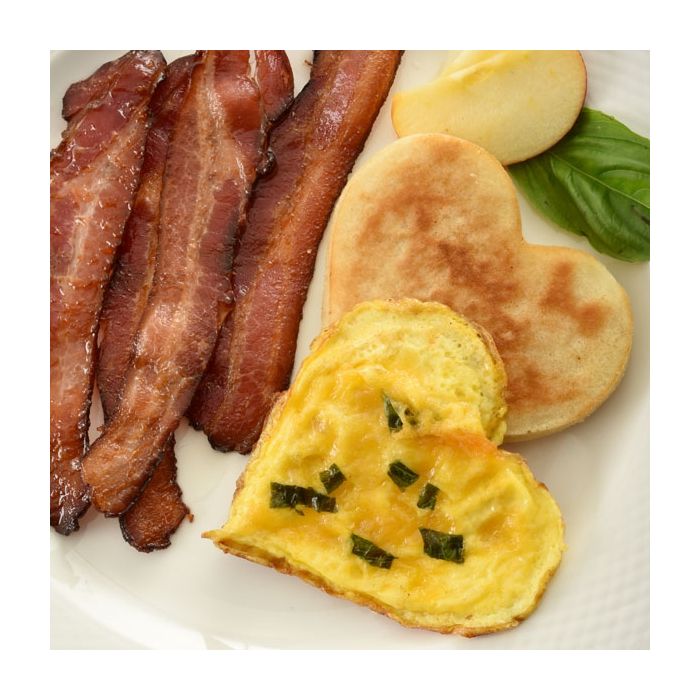 heart shaped egg and pancake on plate with bacon and fruit.