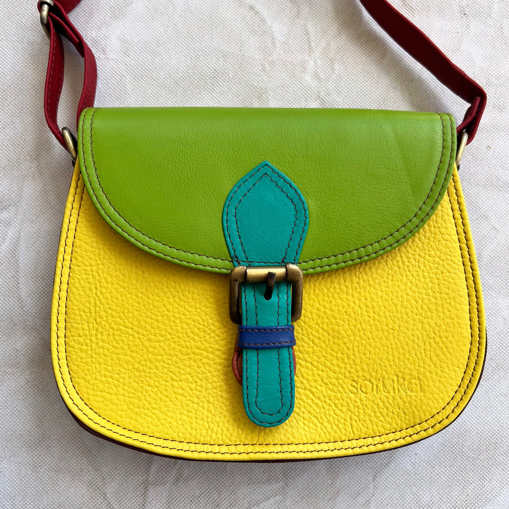 Rounded yellow bag with green flap and blue buckle.