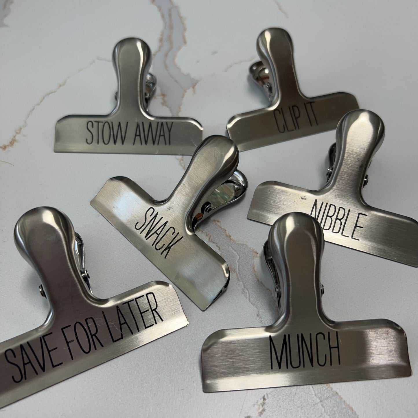 assorted metal bag clips on a white marble countertop,