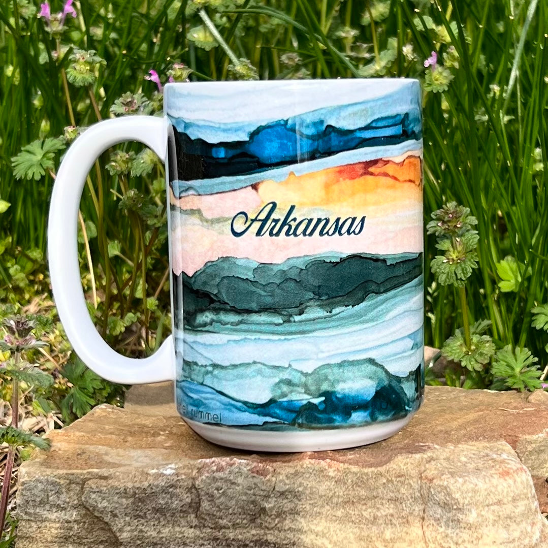 white mug with abstract sunrise design and "arkansas" printed on it.