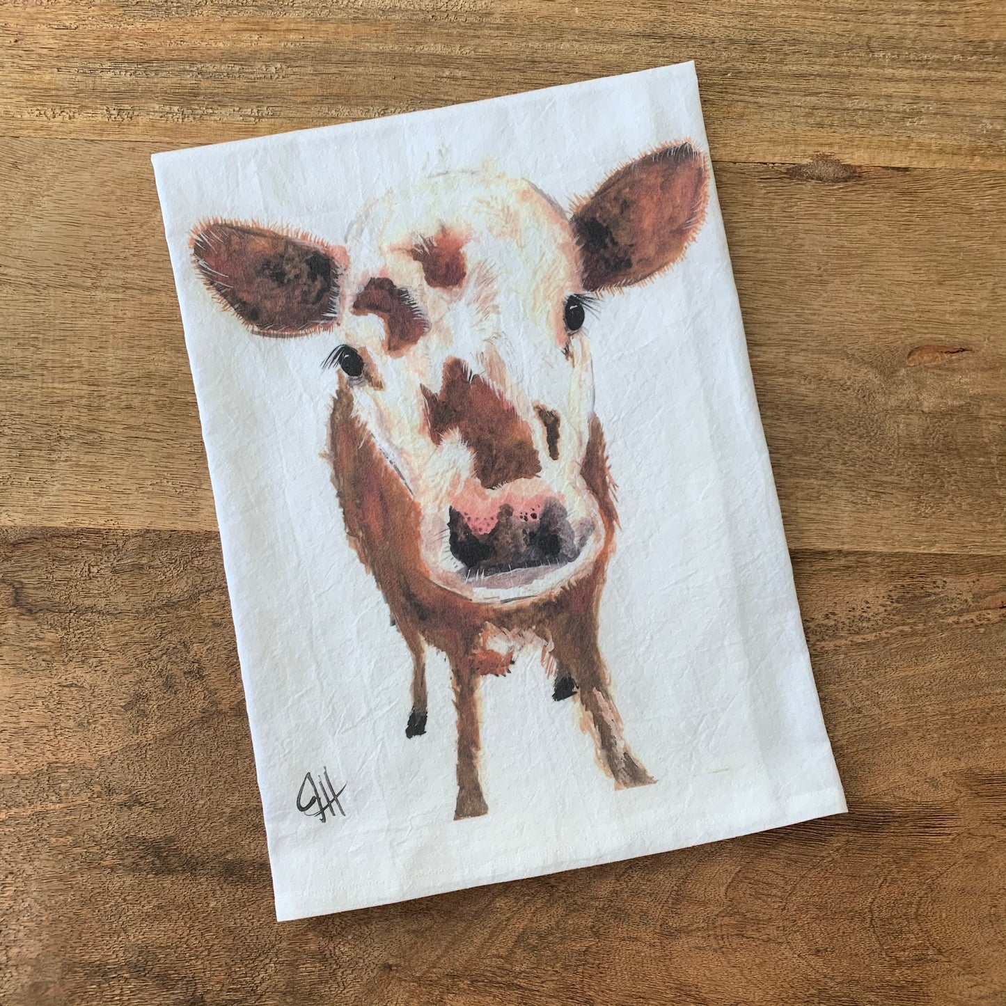 white flour sack towel with a painting of a spotted calf on a wood background