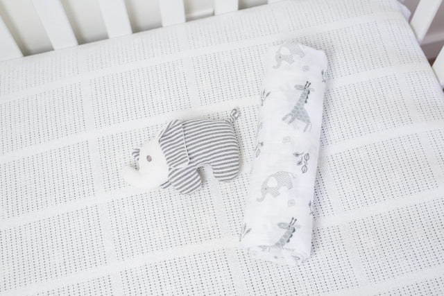 Afrique Cotton Security Blanket rolled up and laying in a crib with a stuffed toy.